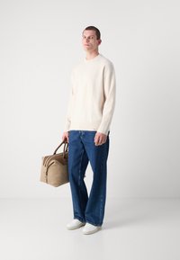 Off-white strikkegenser, avslappet passform; blå vid bukse; hvite joggesko; brun duffelbag med doble håndtak. Glatt tekstur, minimalistisk design.