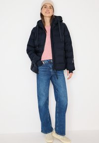 Marineblå pufferjakke med hætte, lyserød sweater og blå straight-leg jeans. Beige sneakers. Enkel design, glat tekstur, afslappet pasform.