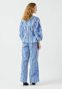 Blå och vit randig outfit med en smockad topp och vida byxor, som har blommönster broderat på byxorna och en texturerad tyg.