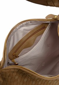 Binnenkant van een tan gekleurde geweven leren tas met een gouden ritssluiting, voorzien van een gladde voering en meerdere vakken, waaronder één met ritssluiting en één insteekvak.