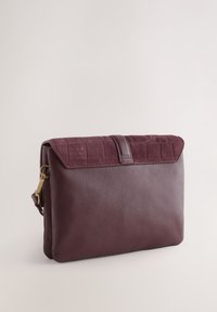 Sac en cuir bordeaux doté d'un rabat en daim texturé, de ferrures dorées et d'une forme rectangulaire, alliant des designs lisses et embossés.
