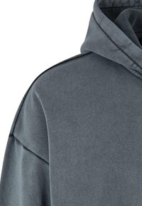 Gros plan d'un sweat à capuche gris montrant la partie supérieure de l'épaule et la zone de la capuche avec des détails de couture visibles.