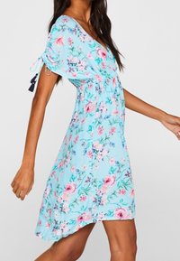 Vestido floral de color azul claro con mangas cortas, decorado con rosas rosas y moradas, cintura ajustada y lazos laterales con borlas. Textura suave.