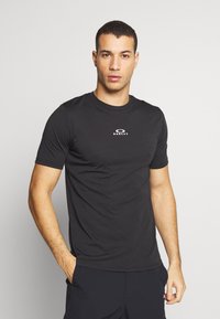 Sort kortærmet t-shirt i en tætsiddende design med et cirkulært logo på brystet og en glat, let stoftekstur.