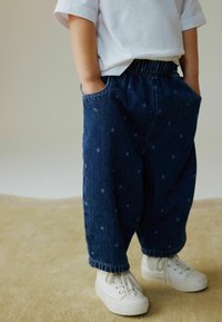 Pantalones vaqueros de corte holgado, con un estampado de lunares, cintura elástica y bolsillos laterales, combinados con zapatillas de lona blancas.