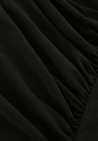 Tissu noir avec une texture douce, présentant des détails froncés et des surfaces lisses qui créent une profondeur subtile.