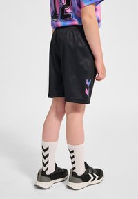 Svarta idrottsshorts med en slät textur, med en rosa och blå logodetalj. Bärs med vita strumpor och svarta sneakers med grå accenter.