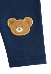 Marinblå leggings med en mjuk bomullstextur, dekorerade med en ljusbrun broderad nallebjörnsapplikation på vänster ben.