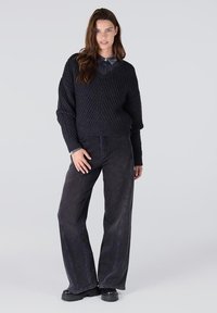 Zwarte gebreide trui met ribbelstructuur en V-hals, gecombineerd met loszittende donkere jeans en dikke zwarte platformlaarzen.