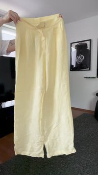 Pantalones de pierna ancha de color amarillo claro, hechos de una tela suave. Cuentan con un cierre frontal, dos pliegues y aberturas en el dobladillo para facilitar el movimiento.