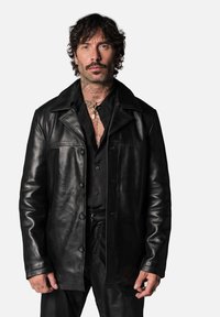 Veste en cuir noir avec un devant à boutons, un col pointu et deux poches poitrine ; présente une texture lisse et une coupe ajustée.