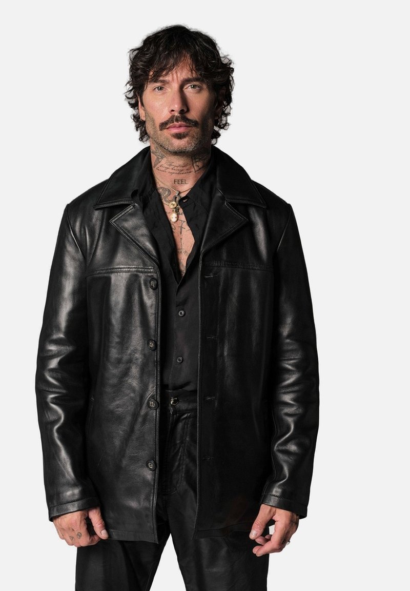 Veste en cuir noir avec un devant à boutons, un col pointu et deux poches poitrine ; présente une texture lisse et une coupe ajustée.