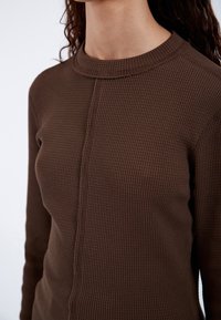 Brown ribbed sweater featuring a high neckline and fitted design, made from textured fabric with visible seam detailing.