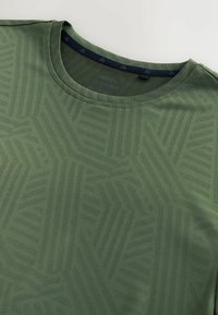 Gros plan d'un t-shirt vert à col rond avec un motif subtil de rayures géométriques et une bande intérieure de col noire.