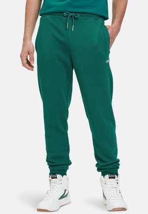 Pantaloni felpa verdi con vita regolabile e coulisse, tasche laterali e polsini a coste, abbinati a sneakers alte bianche con accenti verdi.
