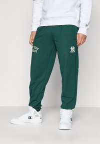 Zaļi kokvilnas joggeri ar "NEW YORK YANKEES" izdrukātiem krēmkrāsas burtiem, ar izšūtu Yankees logo un elastīgām aprocēm. Baltas sporta kedas.