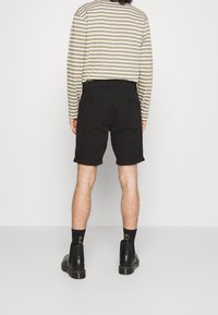 Černé kraťasy s ohrnutými lemy, spárované s pruhovanou košilí s dlouhým rukávem v olivové a bílé barvě. Černé boty s masivní podrážkou.