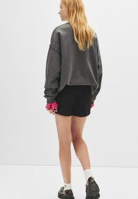 Overmatig grote donkergrijze sweatshirt met gathered mouwen, gecombineerd met zwarte shorts en roze gestreepte mouwen, gedragen met zwarte schoenen en witte sokken.