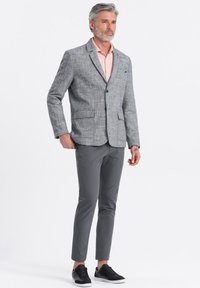 Grå texturerad blazer, rosa skjorta, grå slim-fit byxor och svarta sneakers. Två framfickor på blazern, en knappstängning.