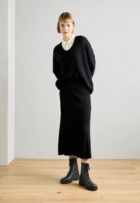 Black knit sweater with a V-neck, paired with a black ribbed skirt and black ankle boots. Smooth texture and minimalist design.