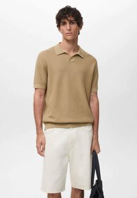 Beige knitted polo shirt with short sleeves, paired with white denim shorts. The outfit is complemented by a black bag.