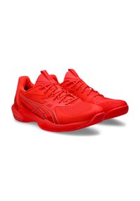 Chaussures de sport rouges avec tige en maille, détails texturés, fermeture à lacets et semelle extérieure en caoutchouc. Présente un design fluide et un renfort au niveau des orteils.
