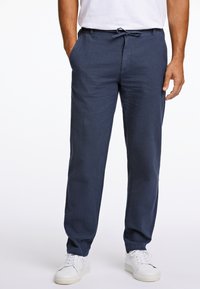 Navy linnen broeken met een relaxte pasvorm, voorzien van een trekkoord in de taille en zijzakken, gecombineerd met witte sneakers.