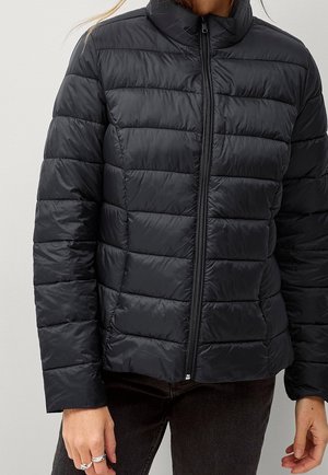 Femme portant une doudoune matelassée noire zippée avec manches longues et col montant.