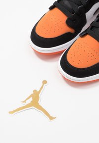 Sneakers neri e arancioni con design perforato, dotati di una intersuola bianca e suola arancione. Include un adesivo con il logo Jordan dorato.