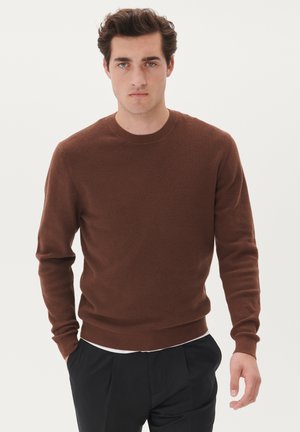 Brown knit sweater featuring a round neck, ribbed cuffs, and a textured pattern, paired with black trousers. Simple, clean design.