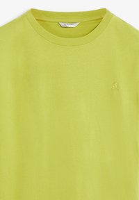 T-shirt à col rond vert lime avec un petit logo brodé de crâne et de tibias sur la poitrine gauche et étiquette de marque Scalpers à l'intérieur du col.