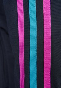 Svart tyg med tre vertikala ränder i rosa, teal och lila. Ytan är slät med en ribbad finish på ränderna.