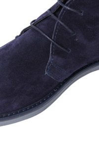 Stivale alla caviglia in camoscio blu navy con punta arrotondata, design con lacci e cuciture blu in contrasto lungo la suola. Texture liscia, decorazioni minime.