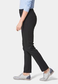 Pantalons en denim extensible noir avec une coupe slim, dotés d'une taille moyenne et d'un design classique à 5 poches, associés à des brogues gris clair.