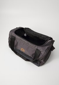 Sac de sport en nylon noir durable avec une fermeture éclair en haut, de larges poignées, un logo orange et un intérieur spacieux. Texture douce, design élégant.