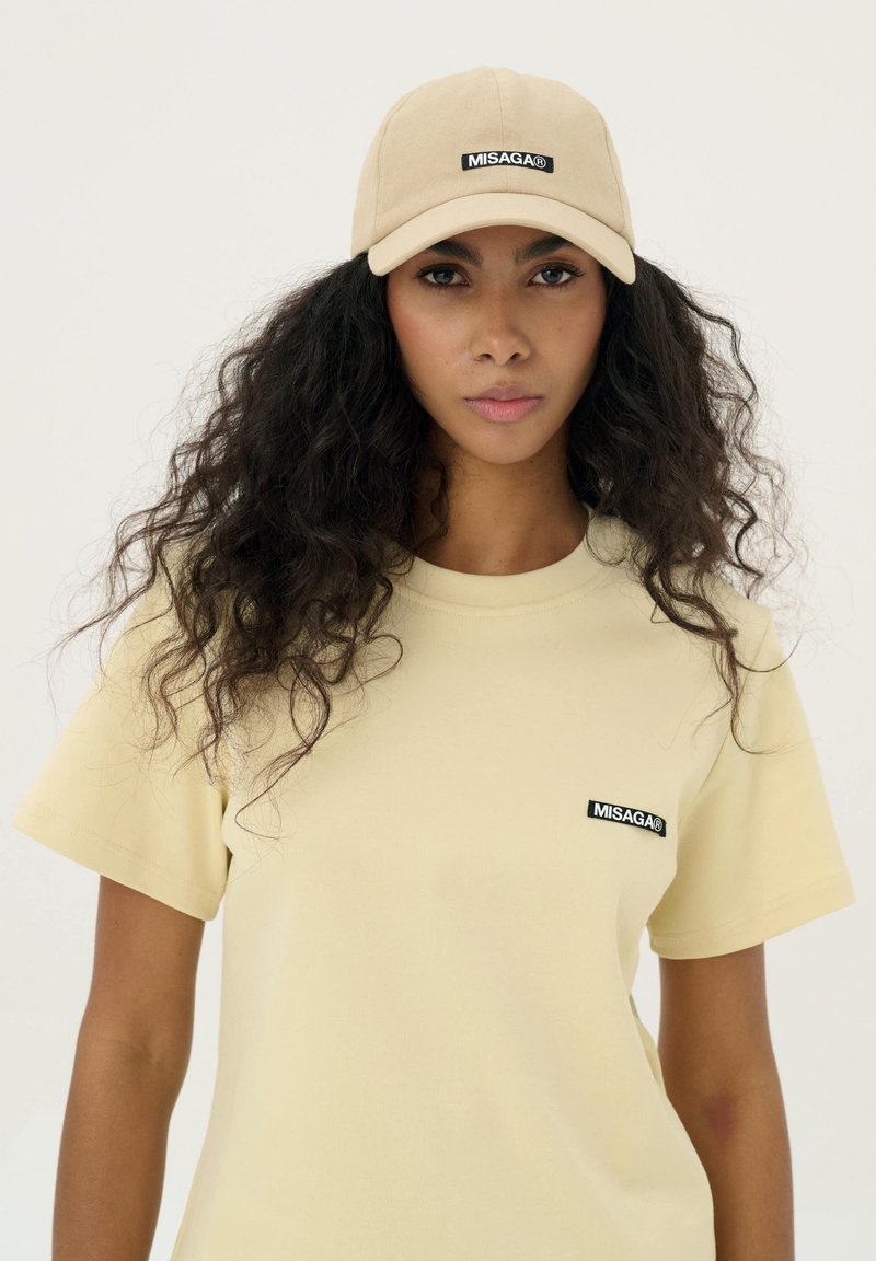 Beżowy bawełniany t-shirt z krótkim rękawem i okrągłym dekoltem, z czarną naszywką z logo. W komplecie z dopasowaną beżową czapką.