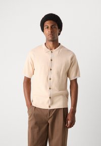 Kortærmet skjorte med krave i lys beige, struktureret stof, der har en knaplukning fortil med runde brune knapper og en afslappet pasform.