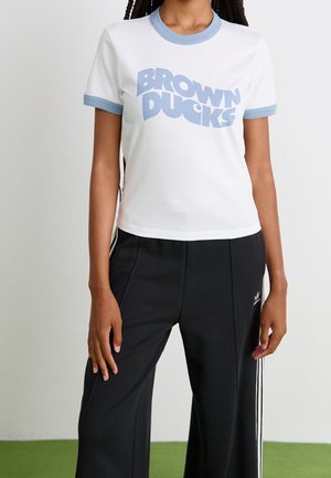 Person iført en hvid T-shirt med blå kant og teksten "BROWN DUCKS", kombineret med sorte Adidas træningsbukser med hvide striber.
