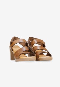 Sandalias de plataforma de cuero marrón con correas cruzadas, un tacón cuadrado y una suela texturizada similar a la madera. Acabado suave y diseño de punta abierta.