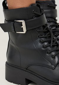 Stivaletto in pelle nera con design allacciato, dettaglio della fibbia laterale, suola robusta e finitura testurizzata per una maggiore aderenza e durabilità.