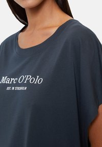 T-shirt blu scuro in cotone, con scollatura ampia e maniche corte. Logo "Marc O'Polo" stampato in bianco. Texture morbida.