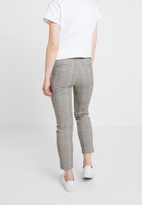 Pantalon à carreaux gris coupe slim, avec une taille mi-haute et des poches arrière, associé à des baskets blanches et un haut blanc court.