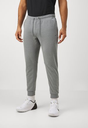Pantalon de jogging gris à coupe fuselée, taille élastique avec cordon de serrage. Comprend des poches latérales et des poignets côtelés. Associé à des chaussures de sport blanches.