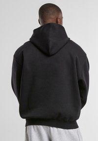 Black hooded sweatshirt featuring a loose fit, ribbed cuffs and hem, and soft fabric texture. Visible stitching and no graphic design.