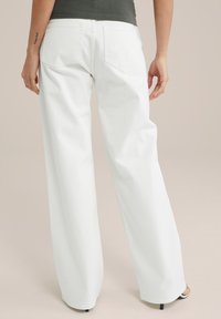 Vita vida jeans i bomull med vida ben, med bakfickor och rak silhuett, bärs med en mörk topp och klacksandaler.