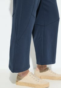 Mörkblå bomullsbyxor med strukturerade sömmar och vida ben, kombinerade med beige kanvas skor med en flätad jute-sula.