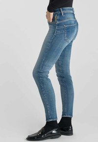 Jeans skinny en denim avec un design classique à cinq poches. Présente un délavage subtil, une taille mi-haute et une ceinture sombre.