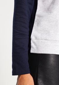 Camiseta de manga larga con una manga azul marino y un cuerpo gris claro, hecha de tela suave, con un diseño sencillo y una silueta ajustada.