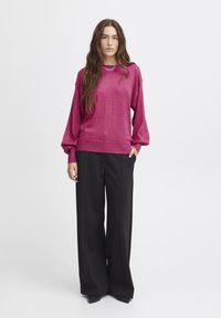 Fuchsia stickad tröja med avslappnad passform, ballongärmar och ribbad nederkant, kombinerad med höga svarta byxor och spetsiga svarta skor.