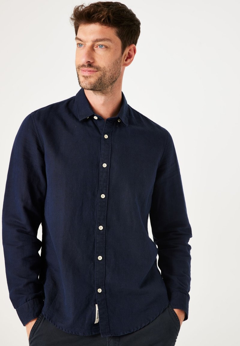 Camisa de manga larga azul marino hecha de una tela texturizada, con un cuello tipo button-down y botones blancos en contraste a lo largo del frente.